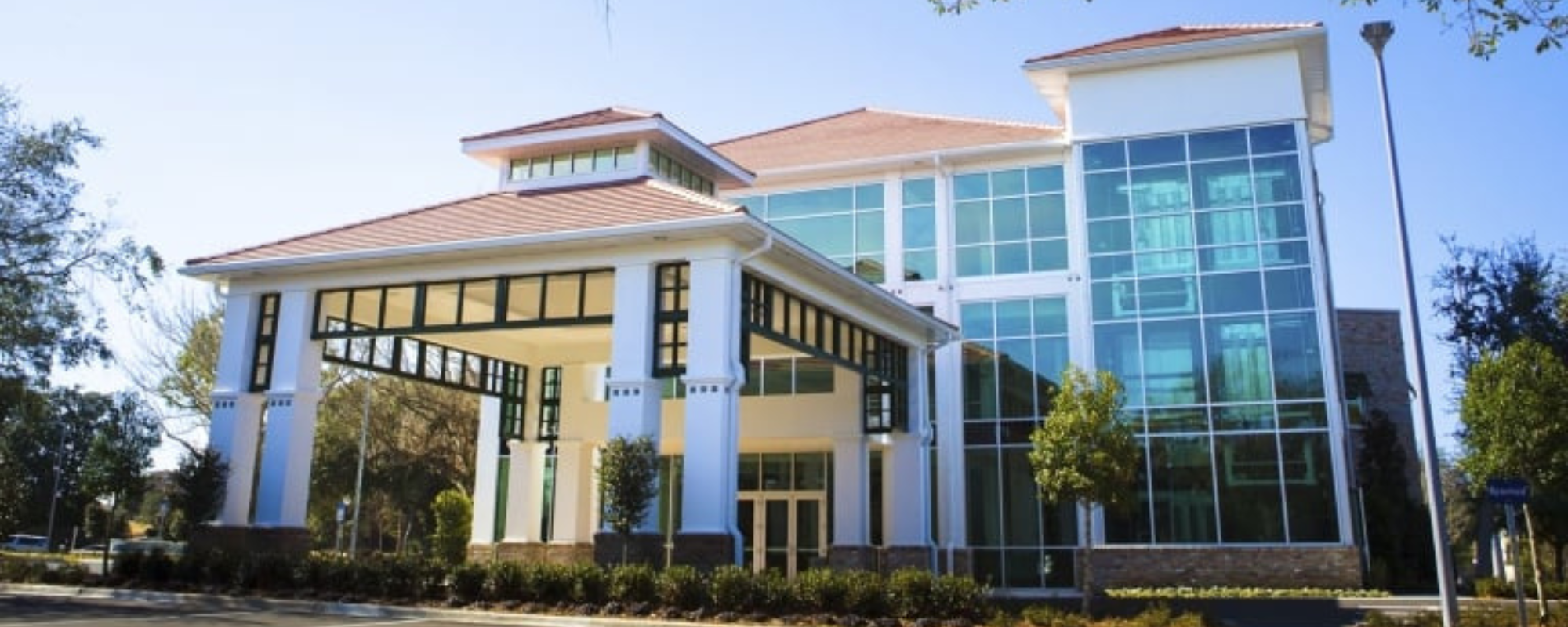 A modern, multi-story building with large windows, located next to a marina with docked boats.