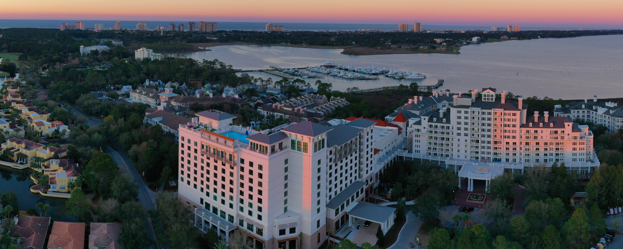 An aerial view of a tall, pink hotel building situated on a bay with a marina.