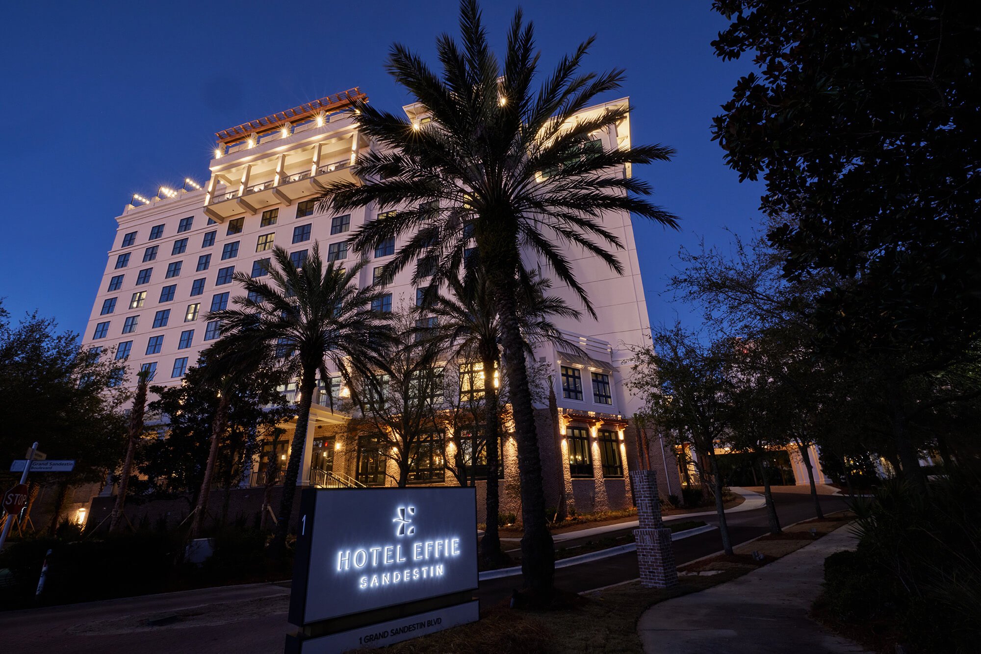 A hotel building and palm trees illuminated at twilight.