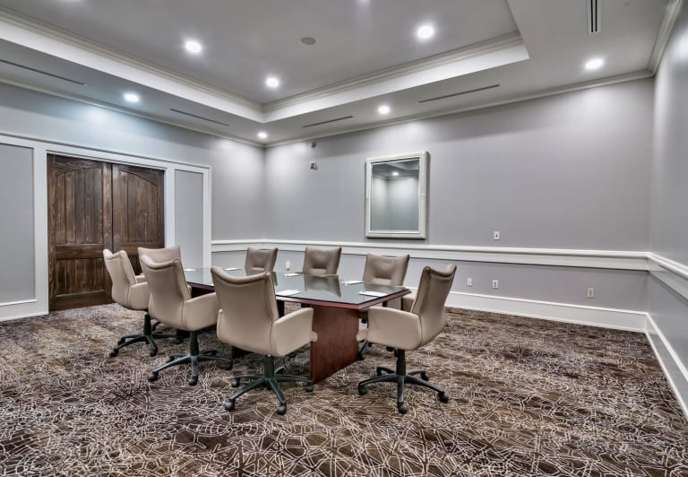 A hotel meeting room set up with chairs and tables, facing a large screen.