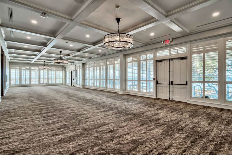 A large, empty hotel ballroom with high ceilings, chandeliers, and floor-to-ceiling windows.