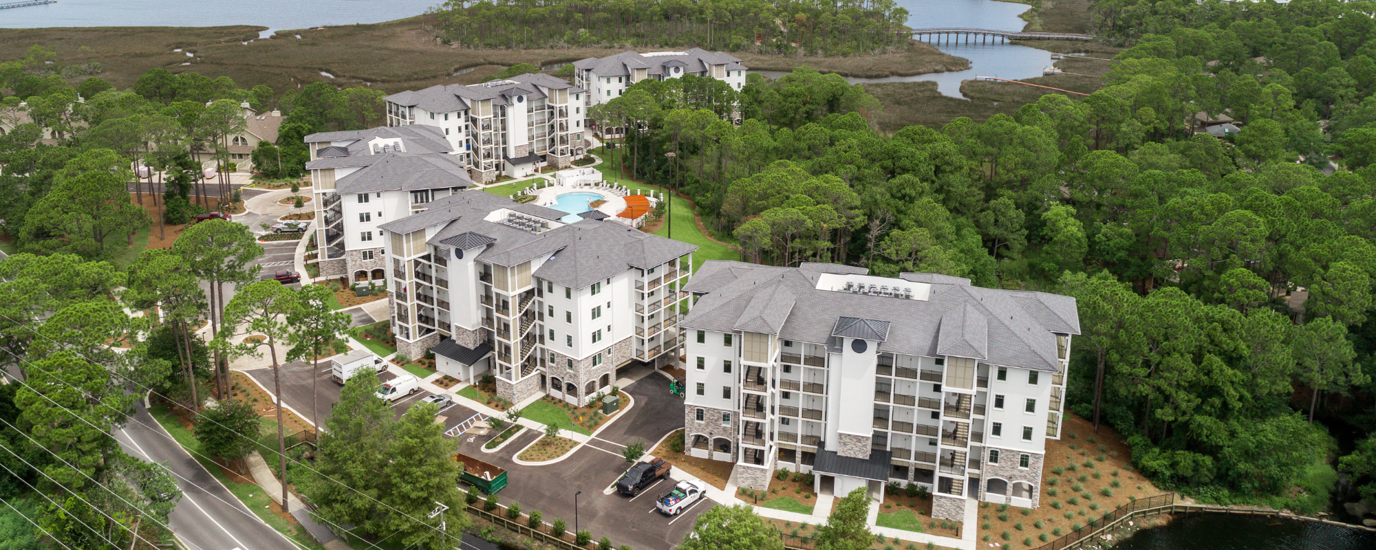 An aerial view of a residential community with multi-story buildings nestled between a marina and a golf course.