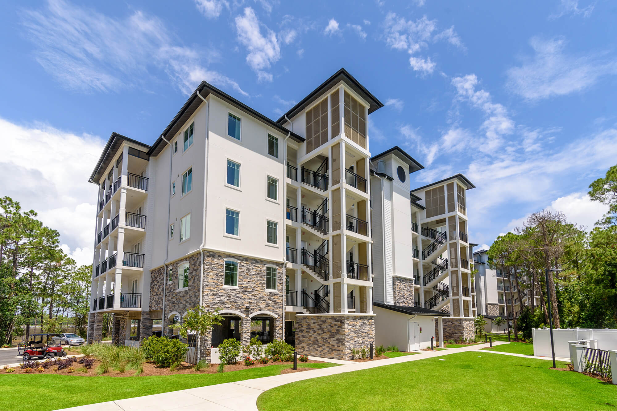 A multi-story condominium building with blue accents and balconies, surrounded by palm trees.