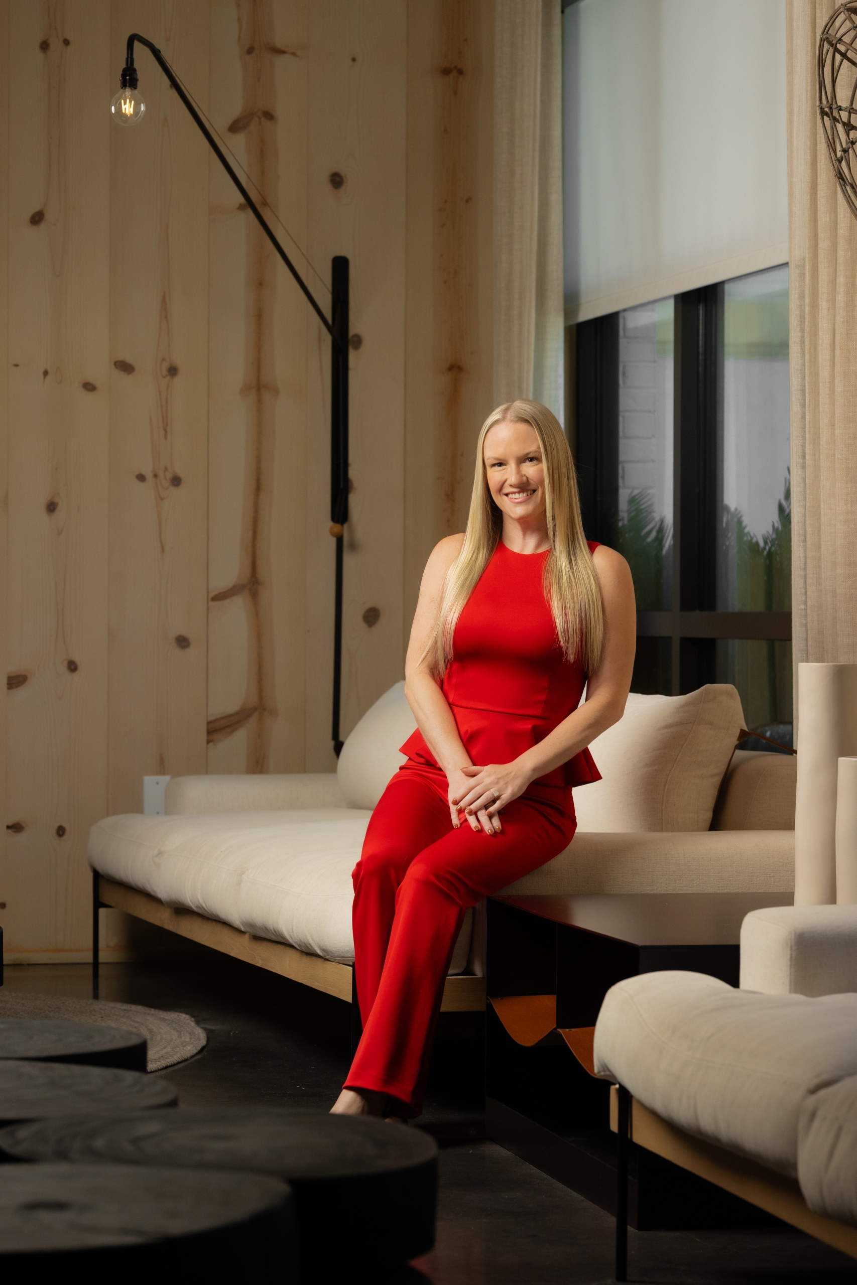 A woman in a vibrant red dress sitting elegantly on a sofa in a well-appointed room.