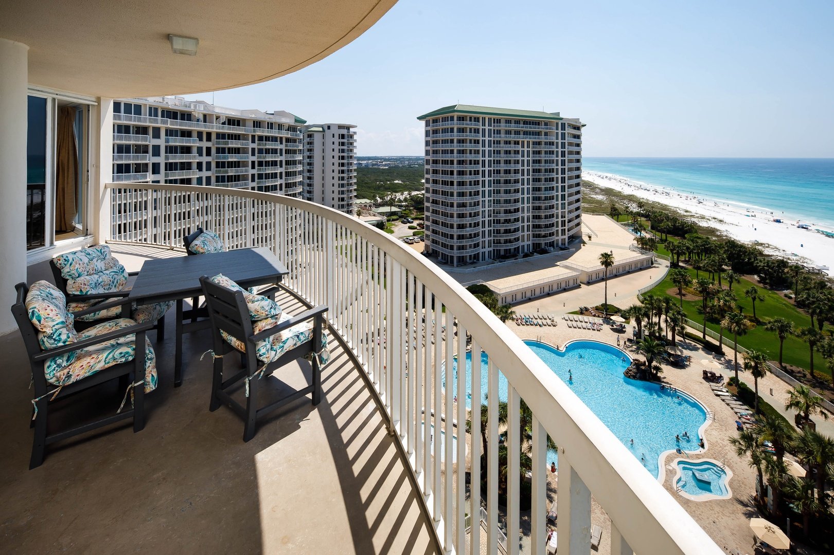 A view from a high-rise balcony looking down at a resort swimming pool and out towards the ocean.