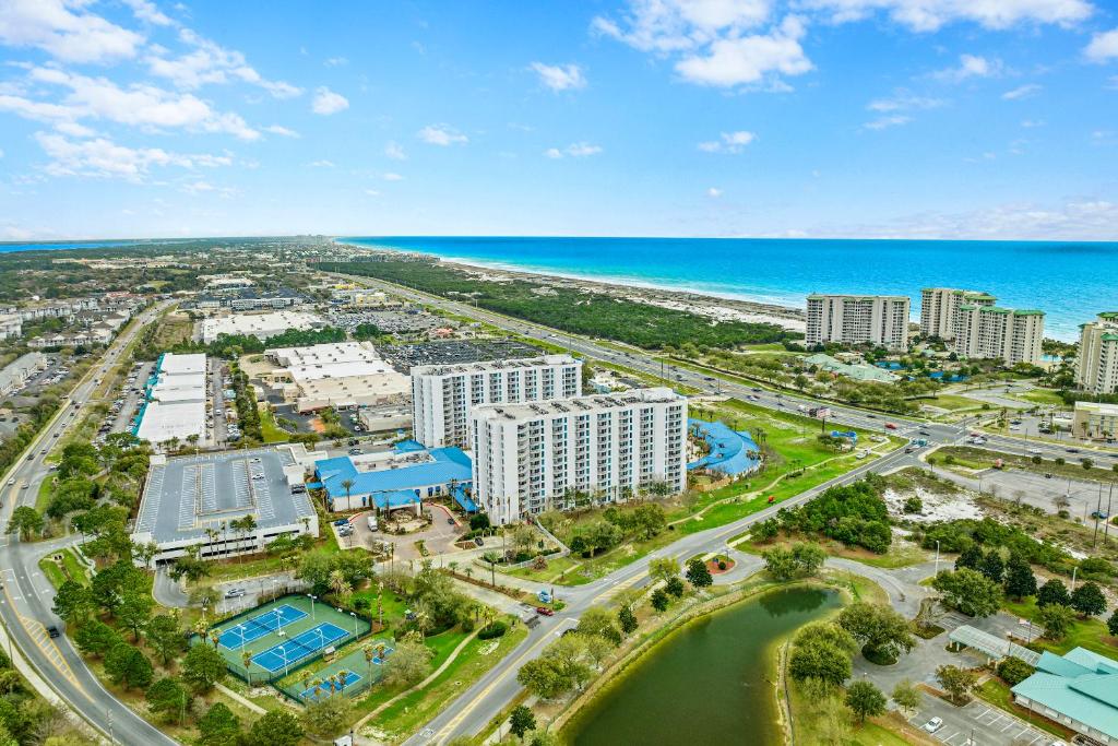 A wide aerial shot of a coastal resort community with lush green landscaping, buildings, and the ocean in the distance.