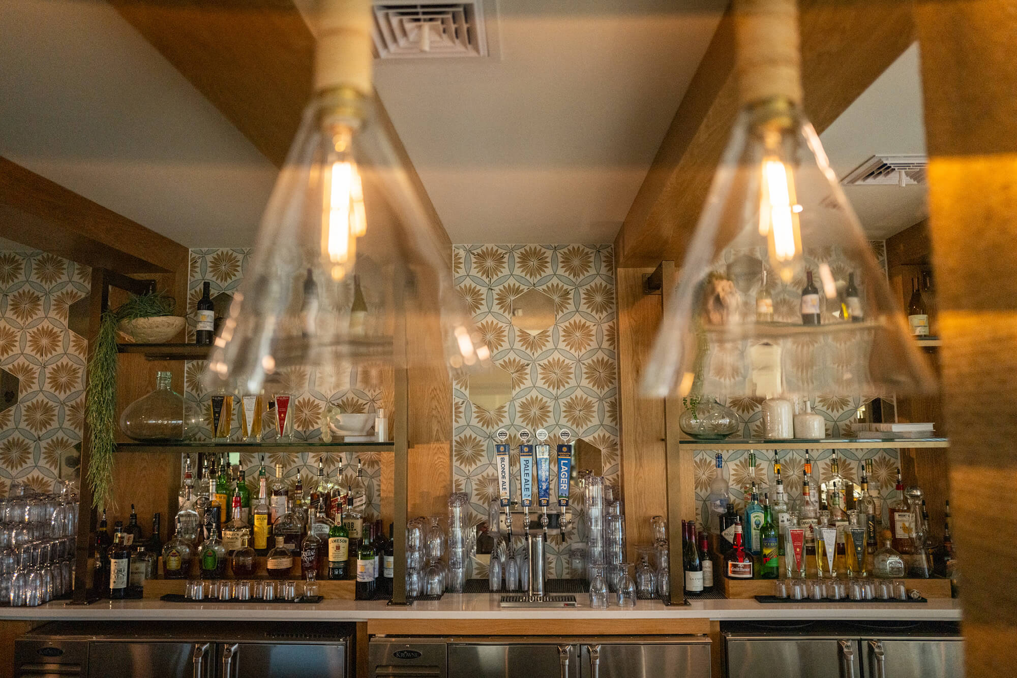 Detailed view of the Beach club bar, with vintage pendant lamps in the foreground and a wall of liquors in the background