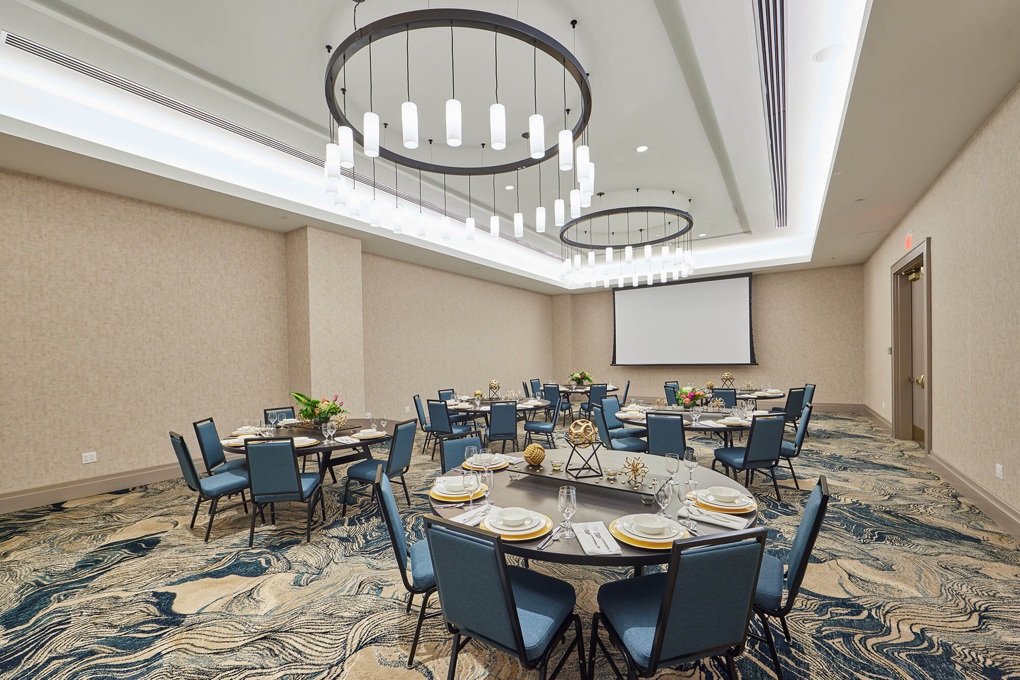A bright open meeting room at the Hotel Effie, with round banquet tables surrounded by chairs, under the light of two large chandeliers