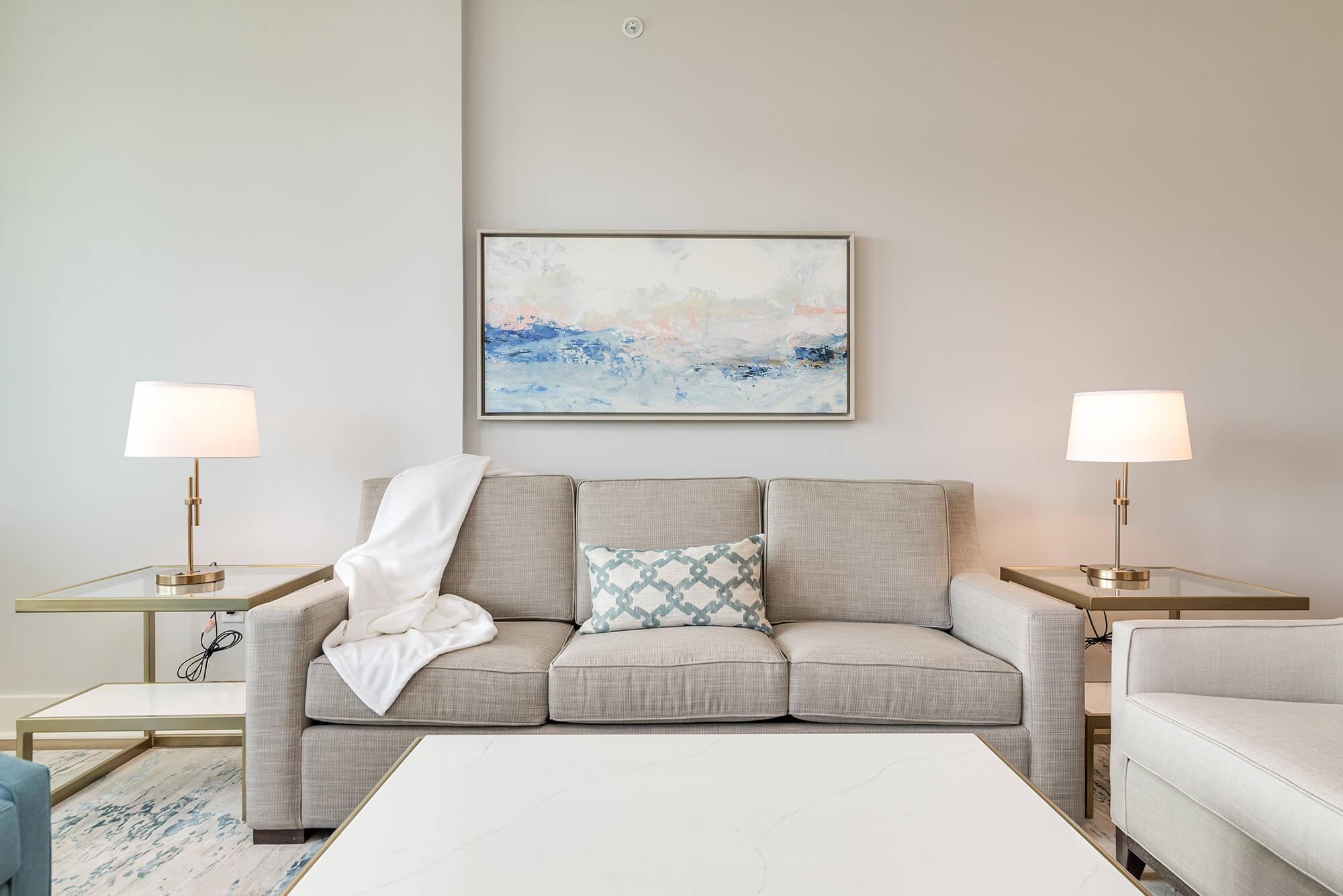 A bright and airy living room and kitchen area with white and blue decor and light wood floors.