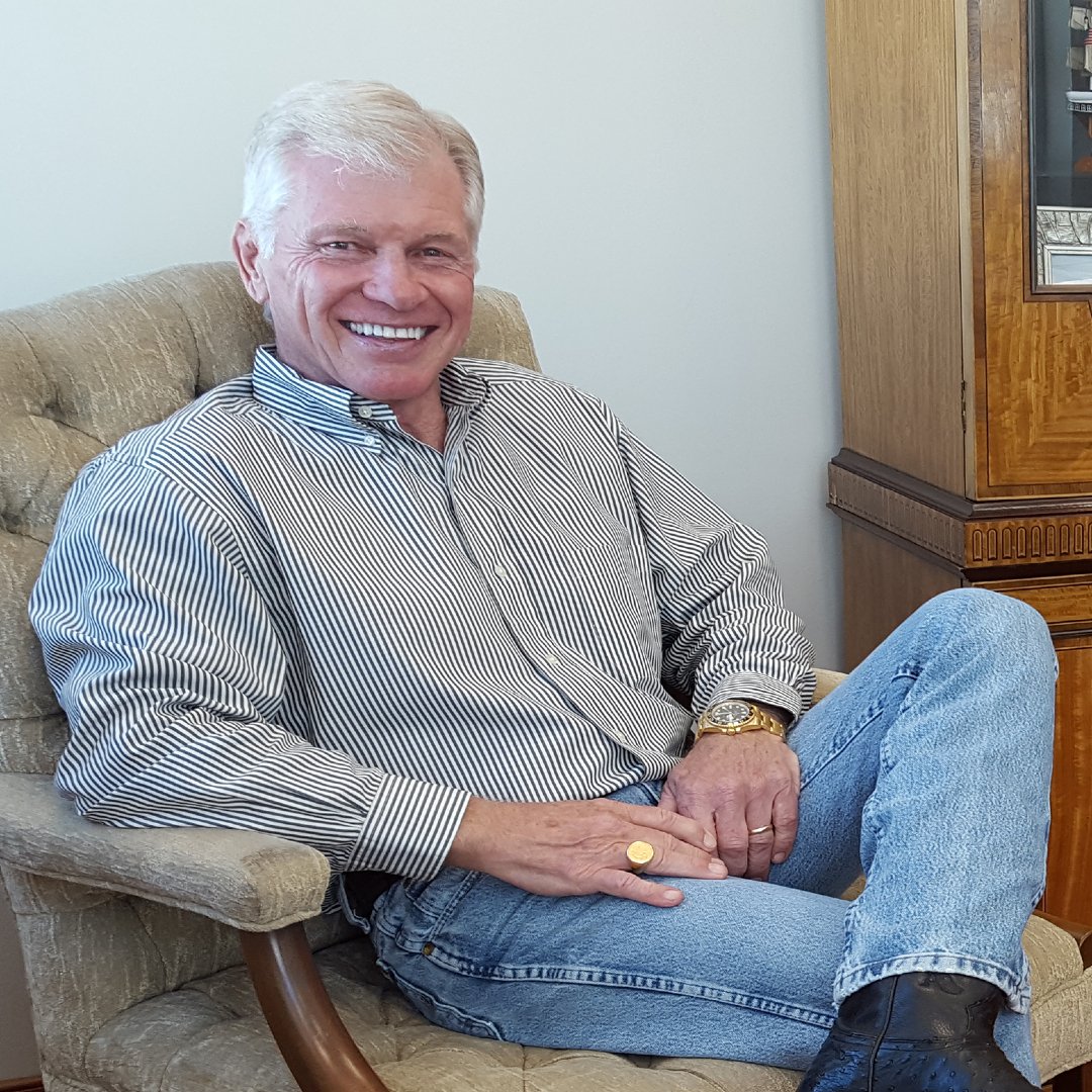A smiling, happy older man sitting comfortably in a chair in a well-lit room.