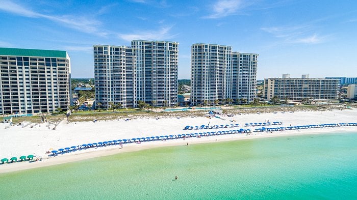 A high-rise condominium building on a white sand beach next to the turquoise ocean.