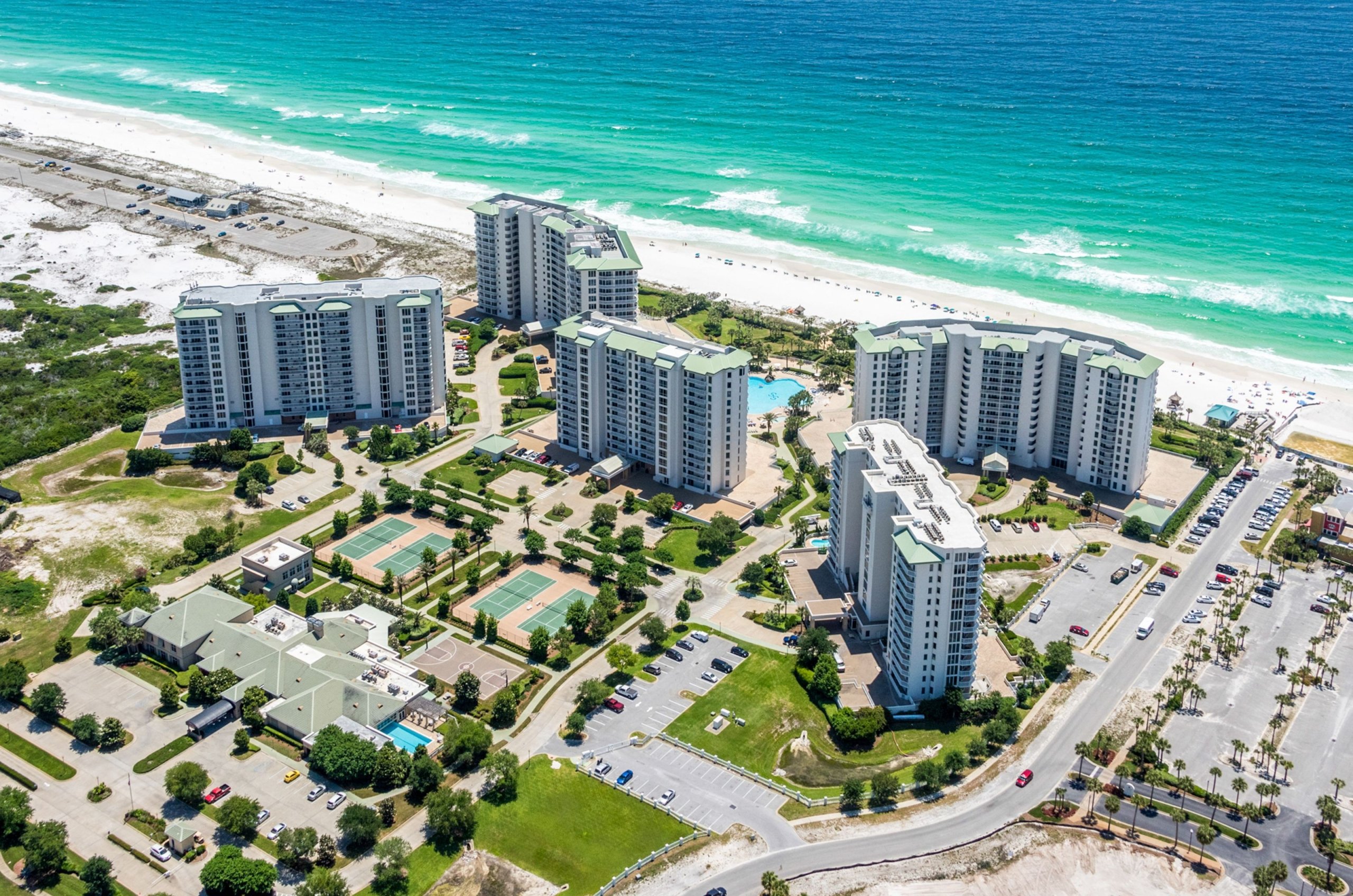 An aerial view looking down the coast, showing multiple high-rise hotels along a white sand beach and turquoise water.