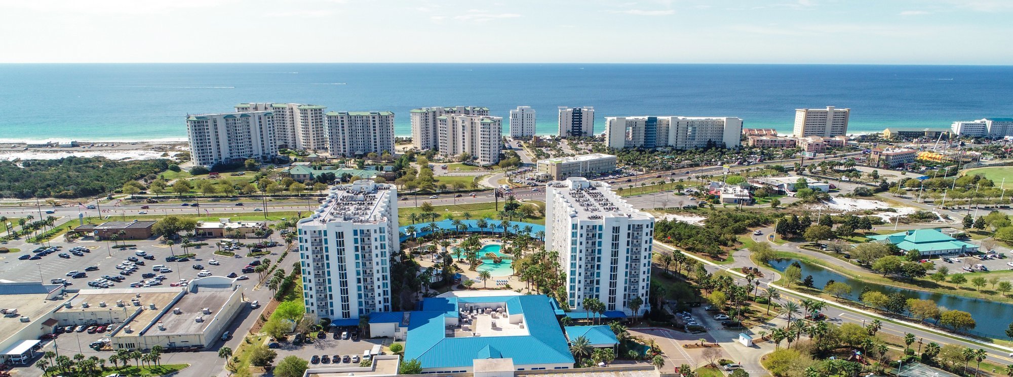 An aerial view looking down the coast, showing multiple high-rise hotels along a white sand beach and turquoise water.