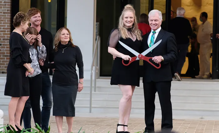A man and woman holding large ceremonial scissors at a ribbon-cutting event.