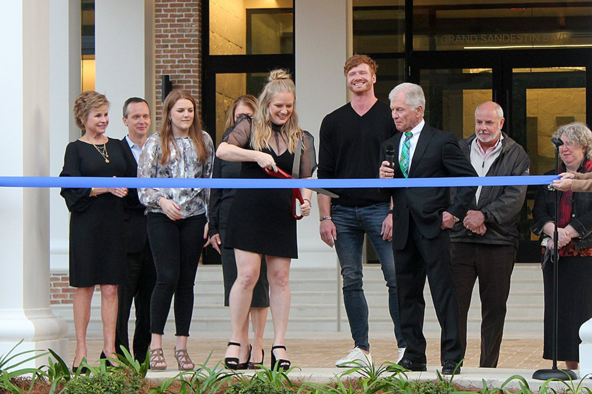 A man and woman holding large ceremonial scissors at a ribbon-cutting event.
